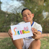 Child holding a watercolor postcard of a colorful cat outdoors