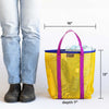 Yellow tote bag with purple handles next to a person, showing dimensions on a white background