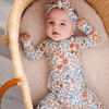 A baby lying on their back inside a woven bassinet, wearing a long-sleeve floral print romper and a matching headband.