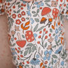 Close-up of a baby's chest wearing a white long-sleeve romper with a colorful print of red-capped mushrooms, blue flowers, green leaves, and orange berries.