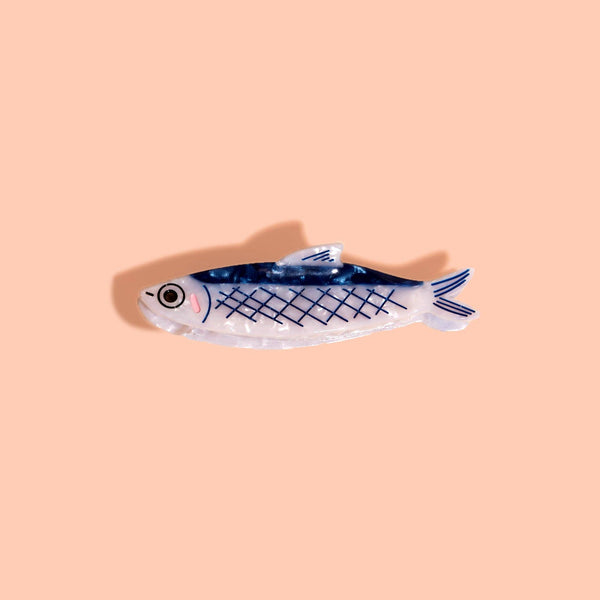 Blue and iridescent white anchovy fish hair claw on a light pink background.