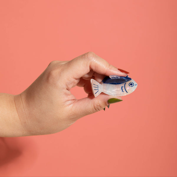 Hand holding a small fish-shaped hair claw against a pink background