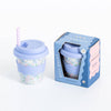 Reusable cup with floral design and blue lid next to its packaging on a white background