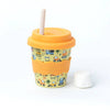 Kid sized travel cup in yellow printed with construction themed motifs, golden yellow silicone wavy grip, lid, and white straw. A marshmallow sits next to the cup against a white backdrop.