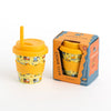 A kid-sized yellow bamboo travel tumbler with a built-in straw and a colorful construction pattern, shown next to its orange and blue CHINO CLUB retail packaging on a white background.
