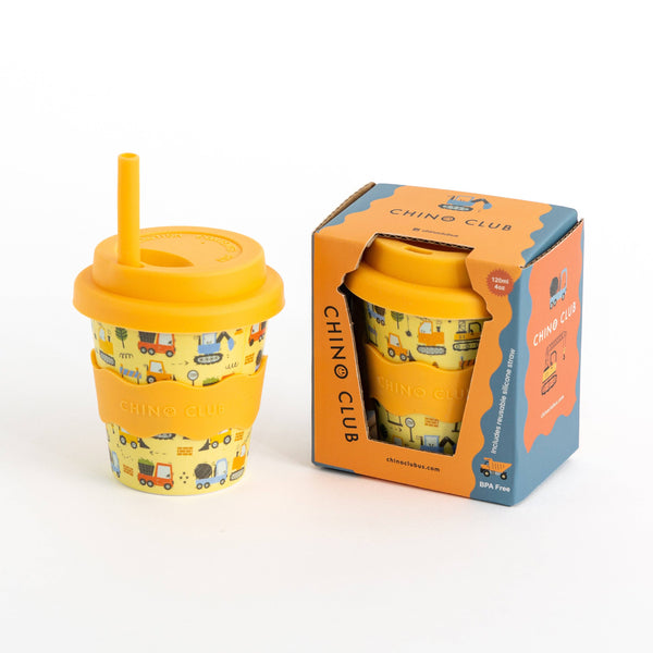 A kid-sized yellow bamboo travel tumbler with a built-in straw and a colorful construction pattern, shown next to its orange and blue CHINO CLUB retail packaging on a white background.