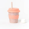 A kid-sized bamboo reusable cup in a pink daisy pattern with pink silicone wavy grip and lid, with straw against a white background. 