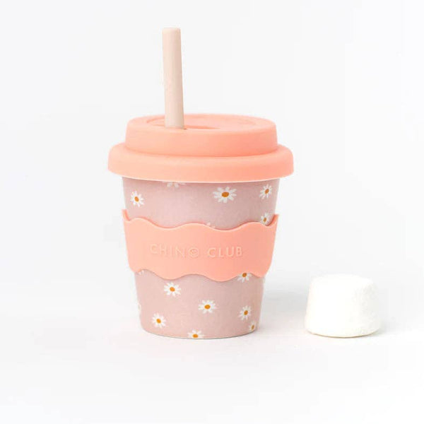 A kid-sized bamboo reusable cup in a pink daisy pattern with pink silicone wavy grip and lid, with straw against a white background. 