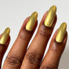 Hand with gold metallic nail polish on a plain background