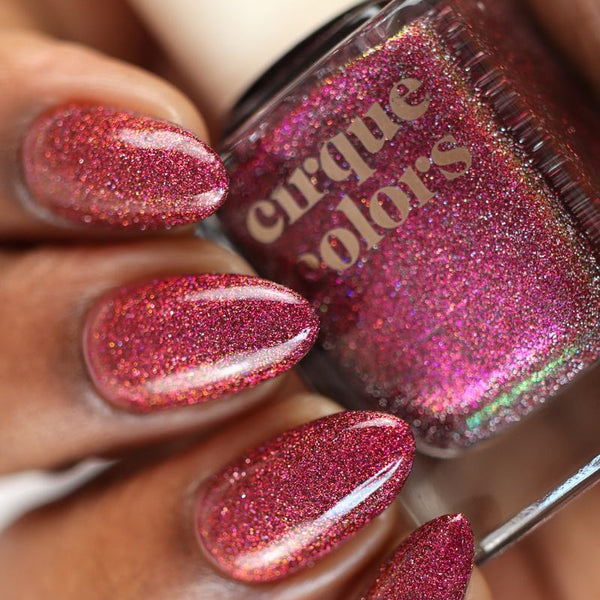 Nail polish with glittery pink color held by a hand, showing close-up of product and application.