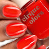 Hand with red nail polish holding a bottle of 'cirque colors' nail polish.