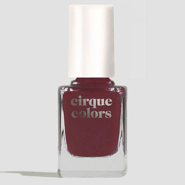 A bottle of Cirque Colors nail polish in a deep mahogany shade, featuring a white cap and clear glass bottle, set against a light gray background.