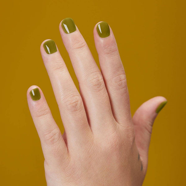 Hand with green nail polish on a mustard yellow background