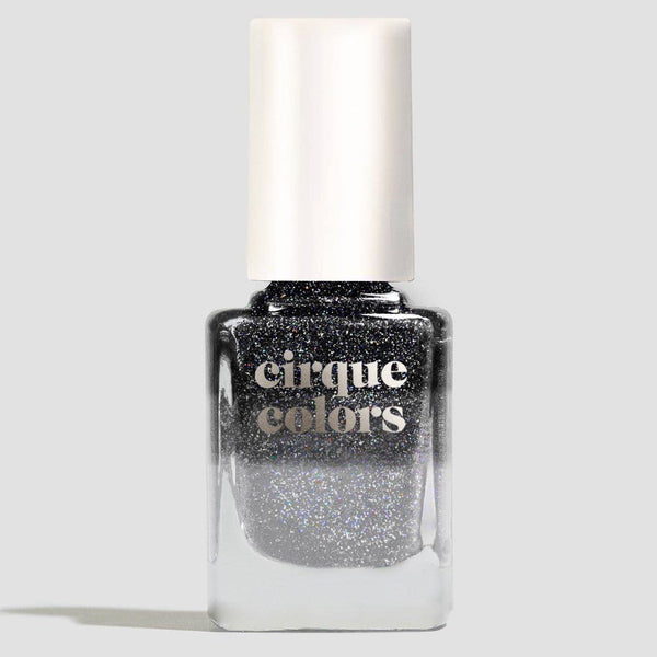 A bottle of Cirque Colors glitter thermal nail polish in a shimmering black-silver shade, featuring a white cap and clear glass bottle on a light gray background.