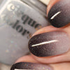 Close-up of fingernails painted with a dark-to-light glitter ombre nail polish, with part of the matching glittery nail polish bottle visible in the background.