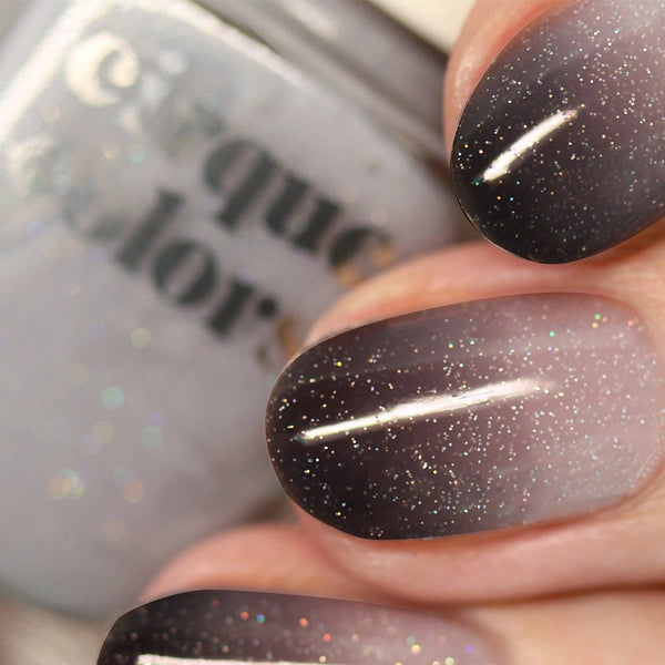 Close-up of fingernails painted with a dark-to-light glitter ombre nail polish, with part of the matching glittery nail polish bottle visible in the background.