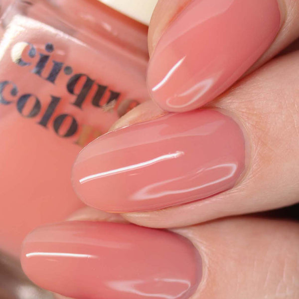 Close-up of a hand with pink nail polish holding a bottle of Cirque Colors nail polish.