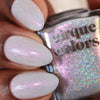 Close-up of a hand with glittery white nails holding a bottle of 'Cirque Colors' nail polish.
