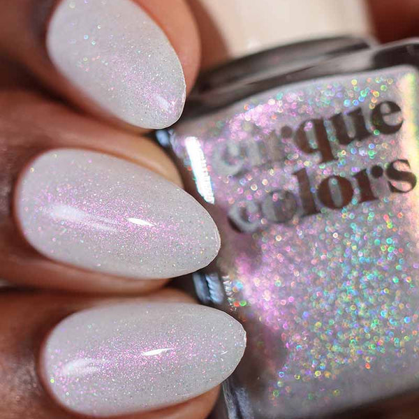 Close-up of a hand with glittery white nails holding a bottle of 'Cirque Colors' nail polish.