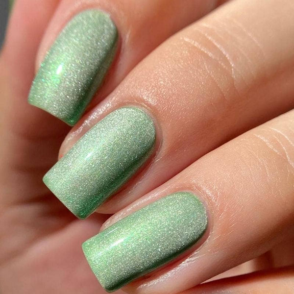 Close-up of a hand with green shimmery nail polish on a neutral background