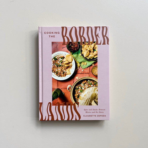 Image of a light pink cookbook with the text "Cooking the Border Lands" by Claudette Zepeda.