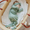 Baby in a green outfit lying in a wicker crib with white bedding.