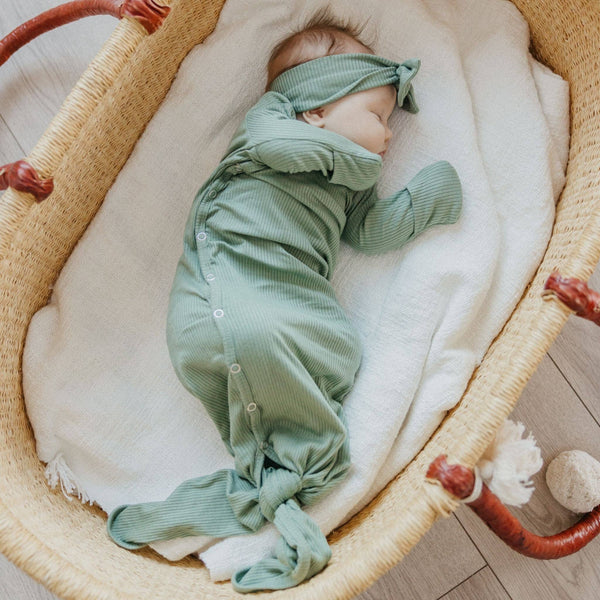 Baby in a green outfit lying in a wicker crib with white bedding.