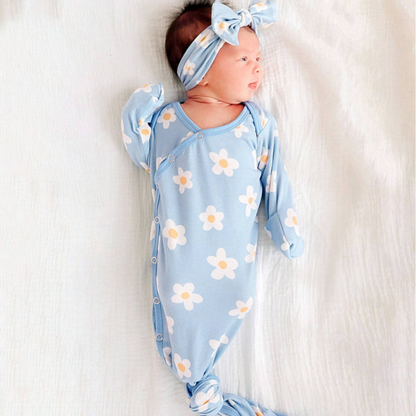 Newborn baby in a blue floral outfit with a matching headband on a white background