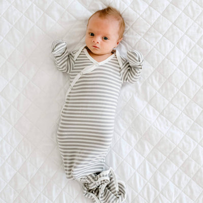 Baby in a striped outfit lying on a white quilted blanket