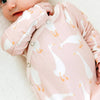 Baby wearing a pink onesie with goose pattern on a light background