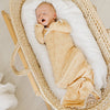 Newborn baby wrapped in a yellow swaddle with smiley face pattern, lying in a wicker Moses basket.