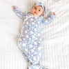 Baby lying on a white blanket wearing a blue floral onesie and headband.