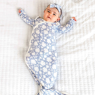 Baby lying on a white blanket wearing a blue floral onesie and headband.