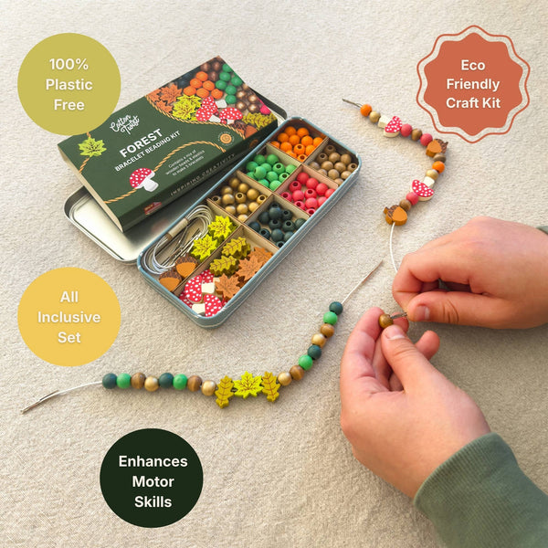 A children's forest-themed beaded bracelet craft kit shown open in a metal tin with multiple color and shape beads, alongside finished beaded strands and a pair of hands actively making a bead necklace. Text callouts around the scene say '100% Plastic Free,' 'Eco Friendly Craft Kit,' 'All Inclusive Set,' and 'Enhances Motor Skills.