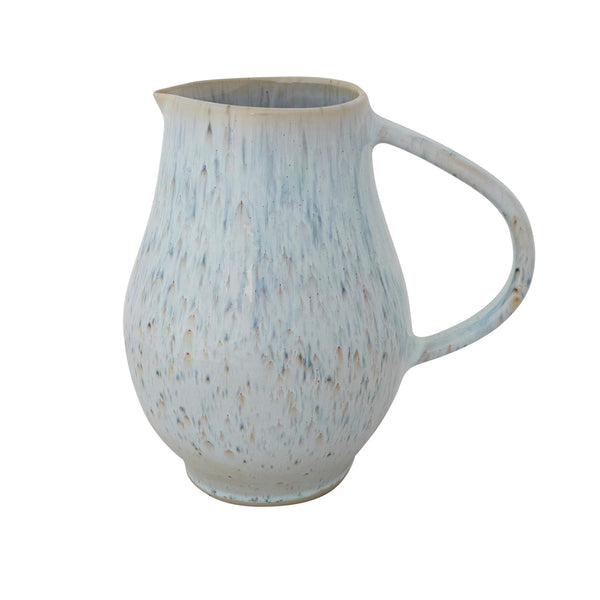 A stoneware pitcher featuring a reactive glaze in light blue tones with brown speckles against a white background.