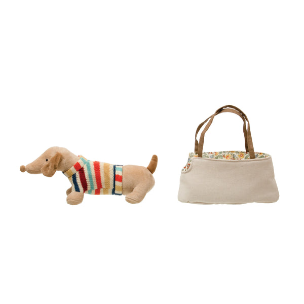 Stuffed dog toy with a colorful sweater next to a small handbag on a white background