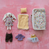 Set of toy clothing and a plush rabbit with a fabric zip suitcase for all the items on a pink textured background