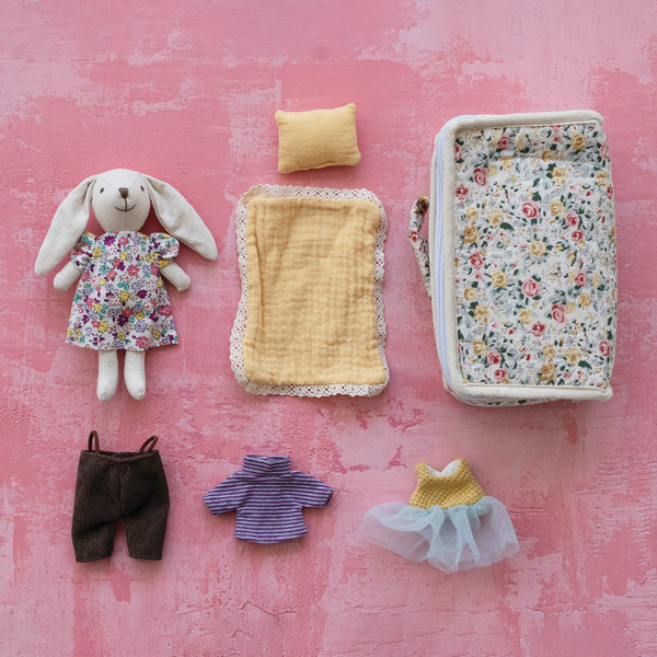 Set of toy clothing and a plush rabbit with a fabric zip suitcase for all the items on a pink textured background