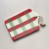 A rectangular stoneware serving board glazed in off-white, red, and green brushstroke plaid with a jute cord handle photographed on a neutral backdrop.
