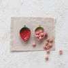 One empty red strawberry shaped dish and one pink strawberry shaped dish overflowing with pink gummy vitamins on a neutral tabletop.