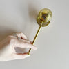 A hand plunging open a gold toned stainless steel tea infuser.