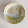 A large low serving bowl in a soft tan featuring a watercolor reactive speckled glaze in a mix of yellow, green and blue against a neutral background.
