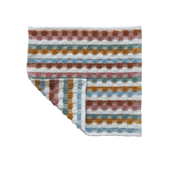 A washcloth with warm colors in a geometric woven pattern with one corner folded back against a white background.