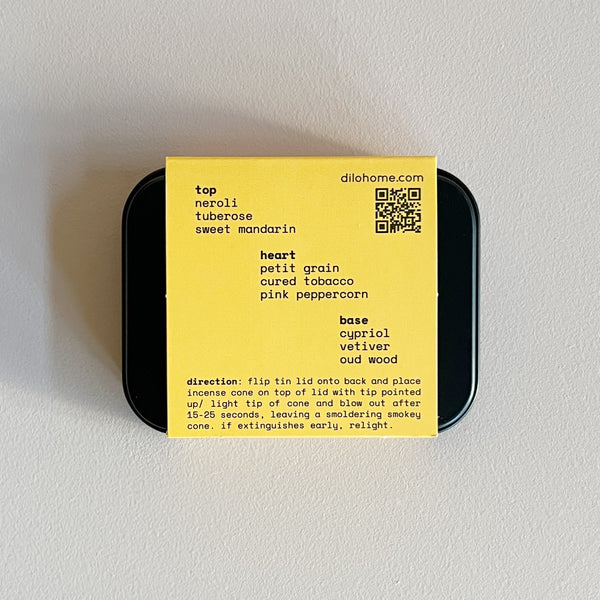 The back of a tin of satsuma oud incense cones, with yellow label listing scent notes and directions, against a neutral background.