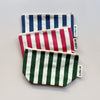 Three organic cotton striped zipper pouches in navy/white, red/white, and forest green/white, layered against a neutral background. 