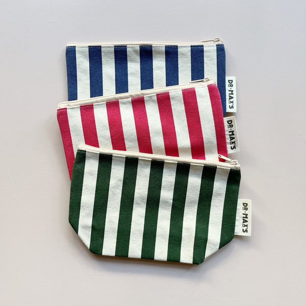 Three organic cotton striped zipper pouches in navy/white, red/white, and forest green/white, layered against a neutral background. 