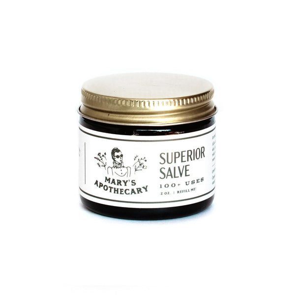 A small amber glass jar of Mary's Apothecary Superior Salve with a gold metal lid and a white paper label, set against a plain white background.