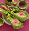 Floral-patterned green napkin with pink flowers on a pink table cloth with ceramic dinnerware. 