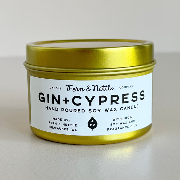 Gold tin candle labeled 'Gin + Cypress' by Fern & Nettle on a light gray background