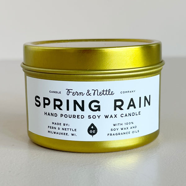 Gold candle tin labeled 'Spring Rain' by Fern & Nettle on a light background